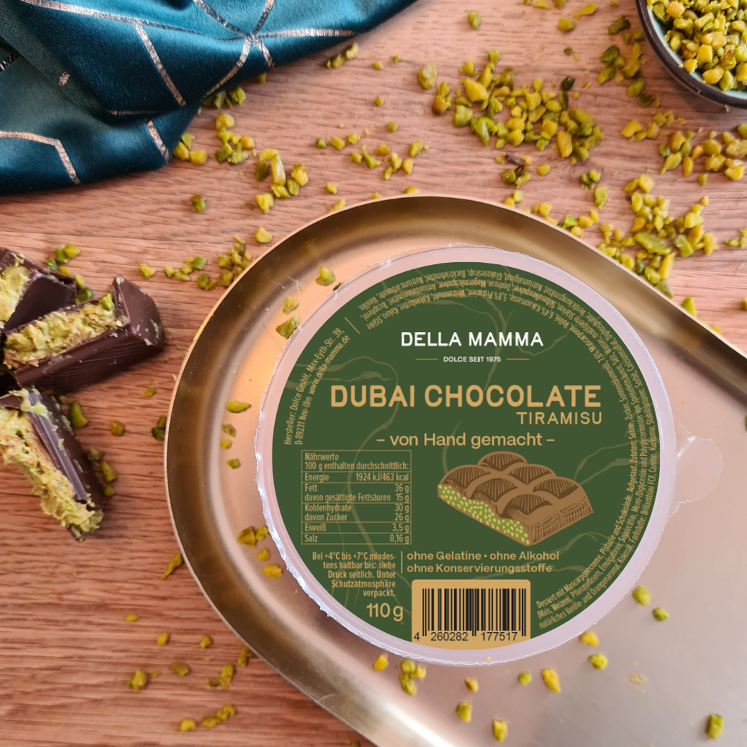 Das Dubai Chocolate Tiramisu im Becher auf einem goldenen Teller dekoriert mit Pistazienkernen auf dem Tisch und richtiger Dubai Schokolade