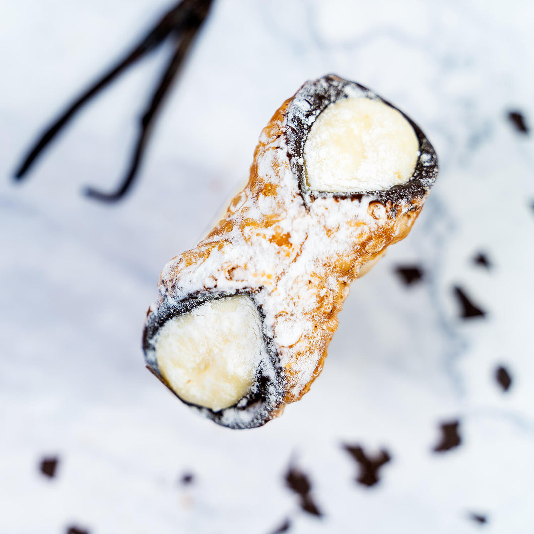 Vanille Cannolo von oben – Frittierte Mürbteigröllchen, innen mit Schokolade ausgestrichen, gefüllt mit Vanillecreme und Puderzucker bestreut 